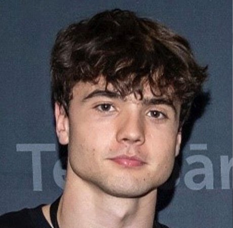 a young man with curly brown hair wearing a black t-shirt and a lanyard