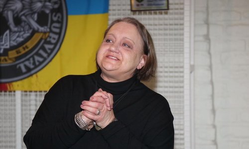 A woman smiling, holding her hands in front of a dancing team flag