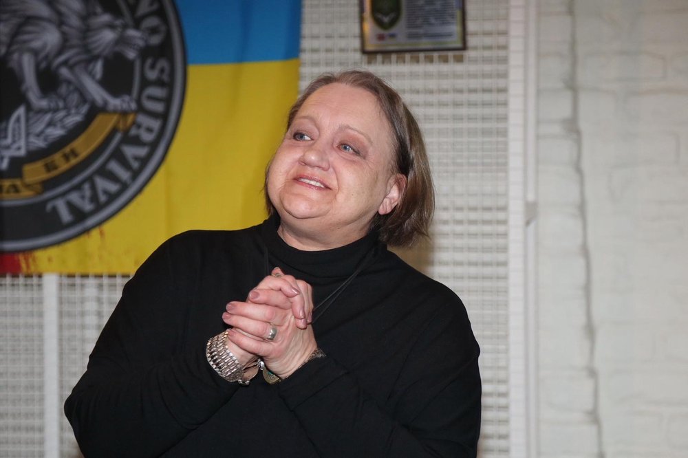 A woman smiling, holding her hands in front of a dancing team flag