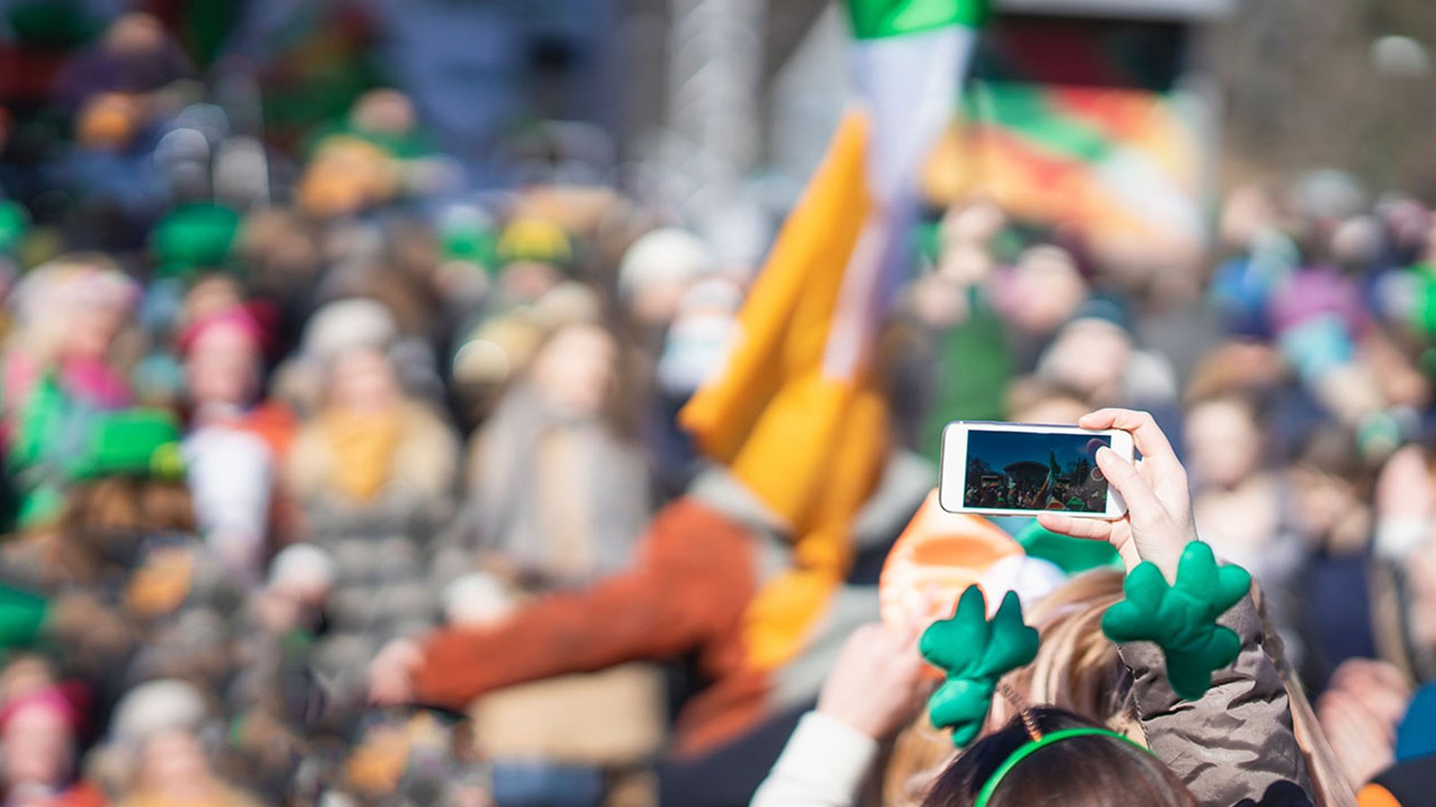 Someone wearing a shamrock headband taking a photo at a St Patrick’s Day parade
