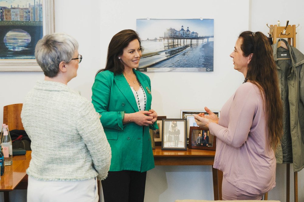 (L-R) Ambassador Maeve Collins, Minister Jennifer Carroll MacNeill and Professor Sabine Asmus stand talking. Professor Asmus' back is to the camera.