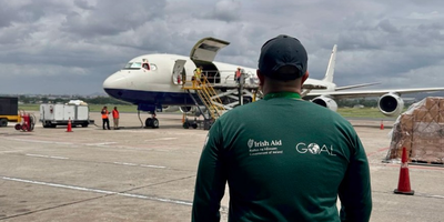 Man in a green t-shirt stands outside airplane delivering aid.
