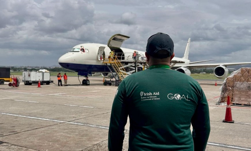 Man in a green t-shirt stands outside airplane delivering aid.