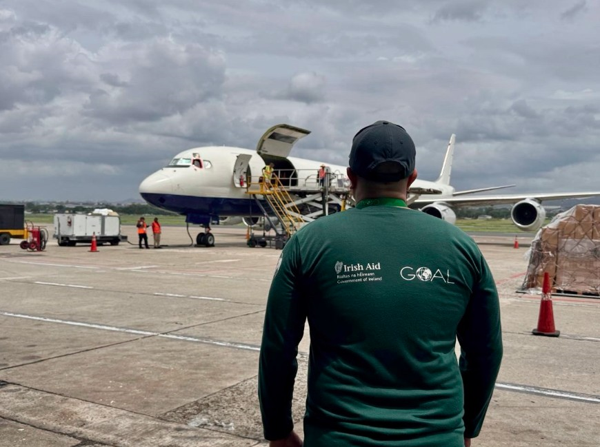 Man in a green t-shirt stands outside airplane delivering aid.