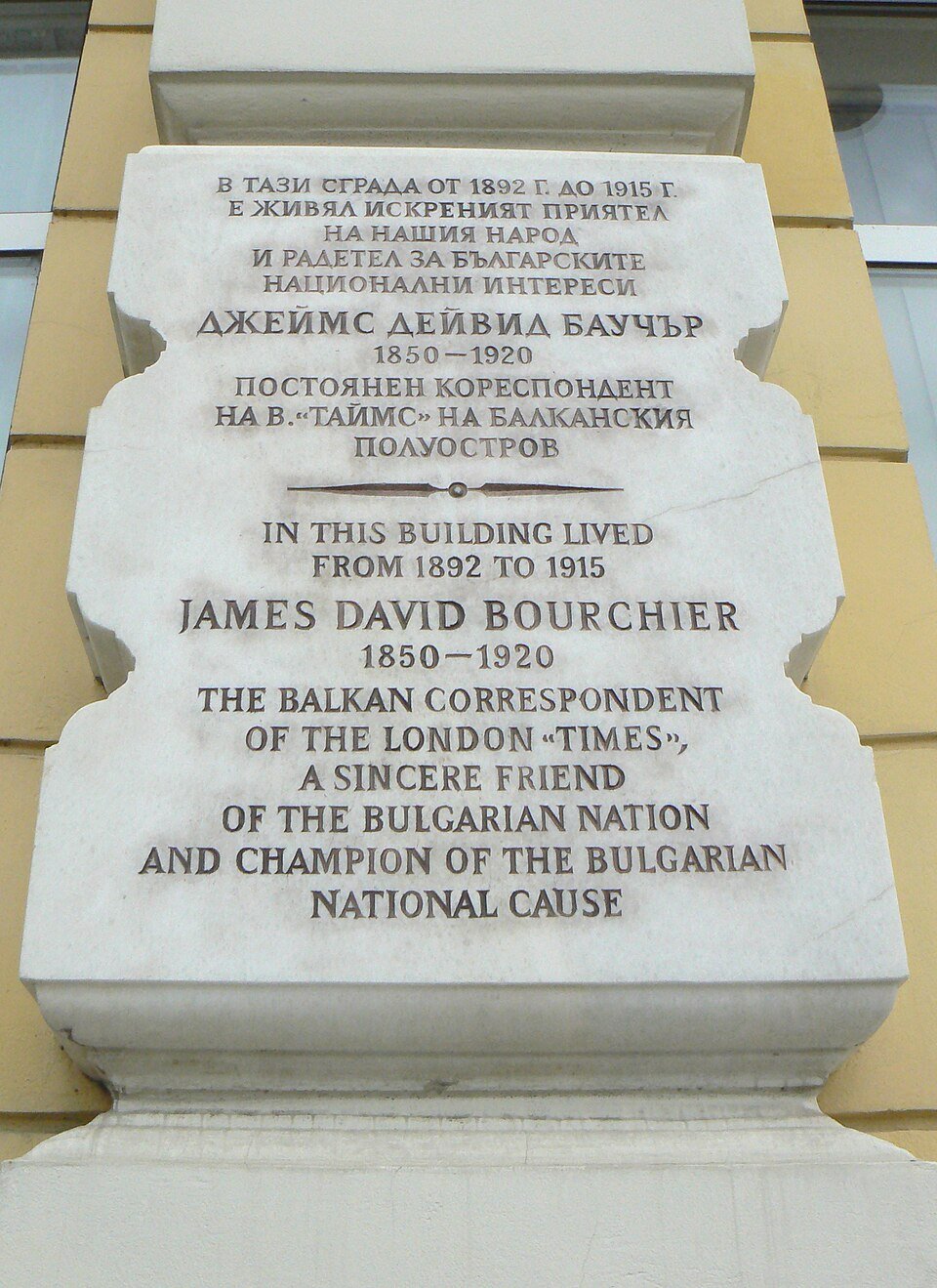 White commemorative plaque on a yellow building pillar