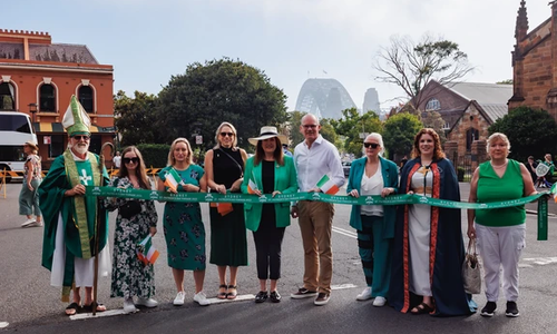people standing in a line holding a green sash outdoors with bridge behind them