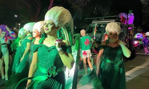 people in green dresses in parade at night time with white wigs shaped like celtic designs