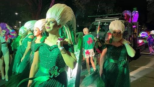 people in green dresses in parade at night time with white wigs shaped like celtic designs