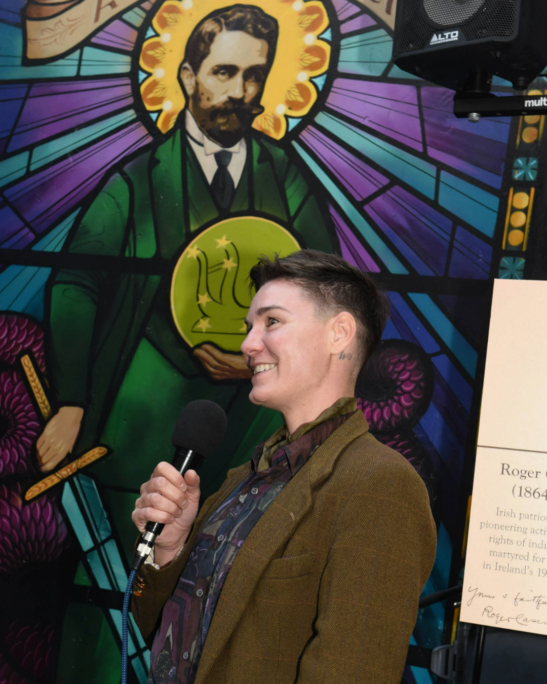 Tanya Wischerath holding a microphone in front of Casement mural