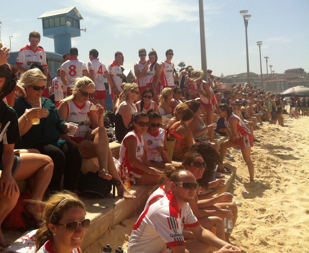 Spectators of a GAA match on Maroubra Beach, they are wearing GAA jerseys and sunglasses