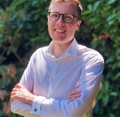 Man wearing glasses and a shirt smiling with his arms crossed