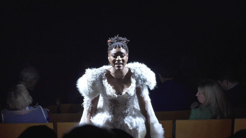 Tolü Makay singer, dressed in a feathery white dress under spotlight with the rest of the stage in darkness