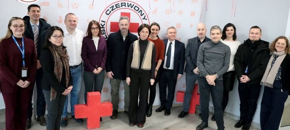 A group of people with a logo of Polish Red Cross in the background