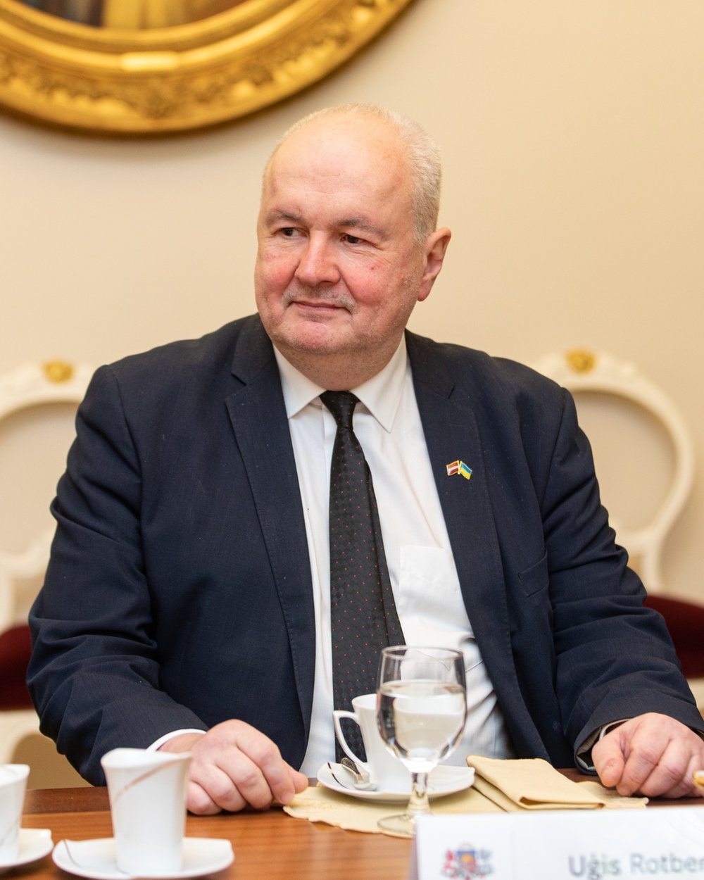 Uģis Rotbergs, sitting at a table in a suit