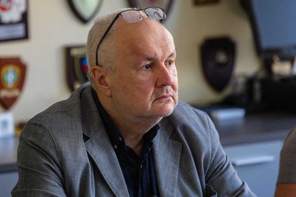 Uģis Rotbergs, looking off camera in a suit and glasses on his head