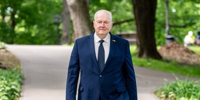Uģis Rotbergs, walking through a park in a suit