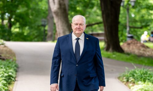 Uģis Rotbergs, walking through a park in a suit