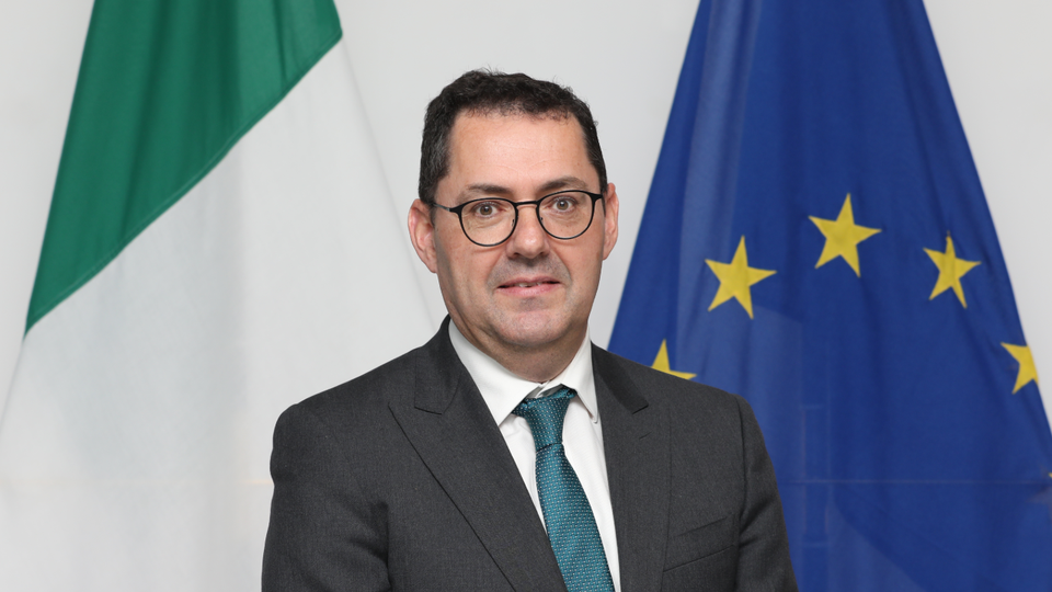 Headshot of the Ambassador in front of Argentinian, Irish and EU flags.