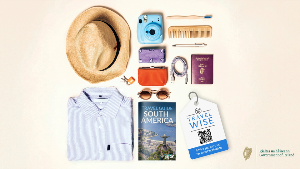 Flatlay of objects to be packed when going on holiday, including Irish passport, travel guide and DFA travel advice