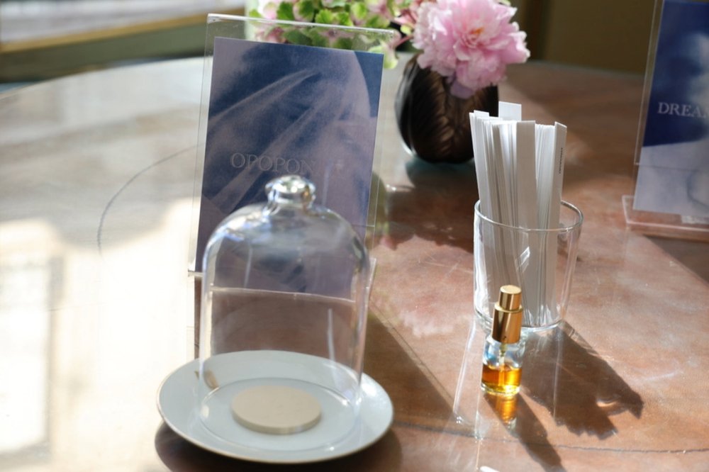 A bottle of perfume beside a bell jar containing a sample of the scent. Test strips are displayed beside them inviting people to try it.