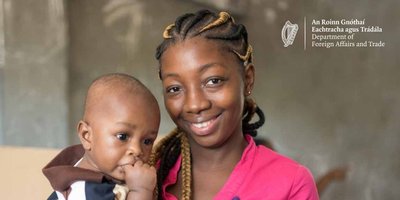 A woman holding a baby in front of a blackboard