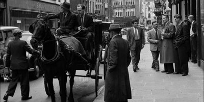 Patrick Kavanagh pointing from carriage towards man on street, Anthony Cronin seated alongside him, jarvey and group of men gathered outside Davy Byrnes, Bloomsday, Duke Street, Dublin