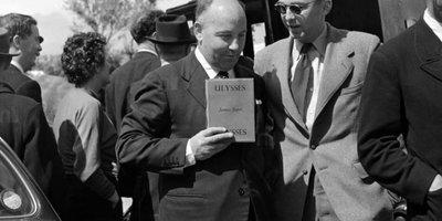 Unidentified man holding copy of "Ulysses", others in background, Michael Scott's house, Sandycove, Co. Dublin