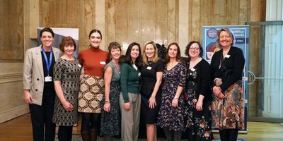 A group of adults stand in a row looking at the camera. In the background is a beige-coloured alabaster and marble wall.