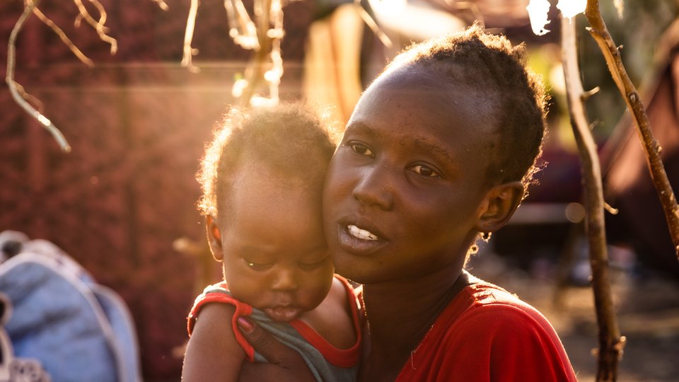 A woman holds a baby in her arms as the setting sun shines on them.