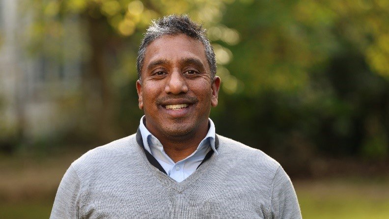 Man smiling at the camera with foliage in the background