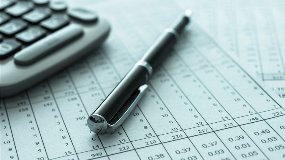 fountain pen lying on top of pages of typed numbers in columns beside a computer keyboard