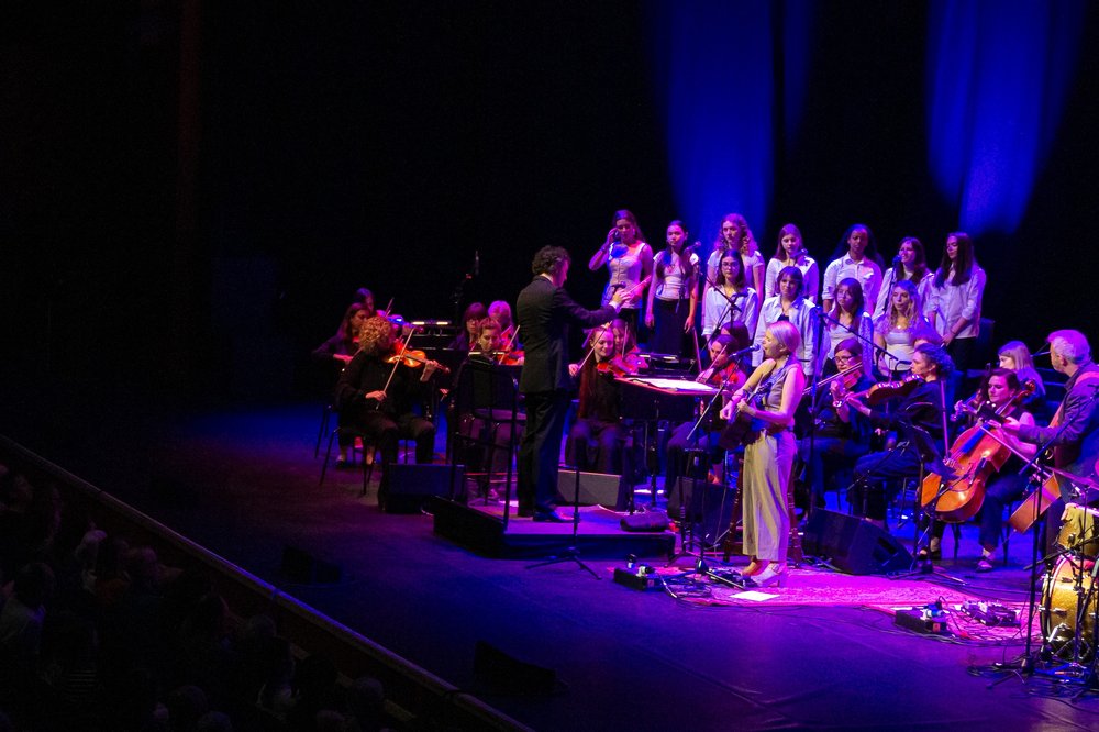 Aoife O'Donovan performing on a stage with a choir and piano