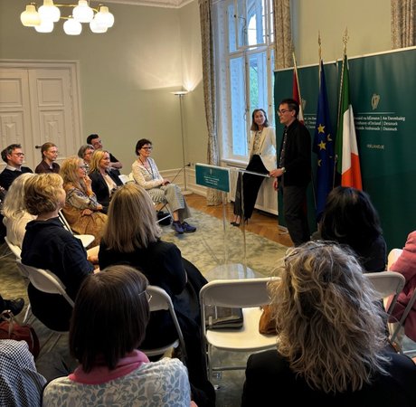 audience watching a man and woman give a talk in large embassy room
