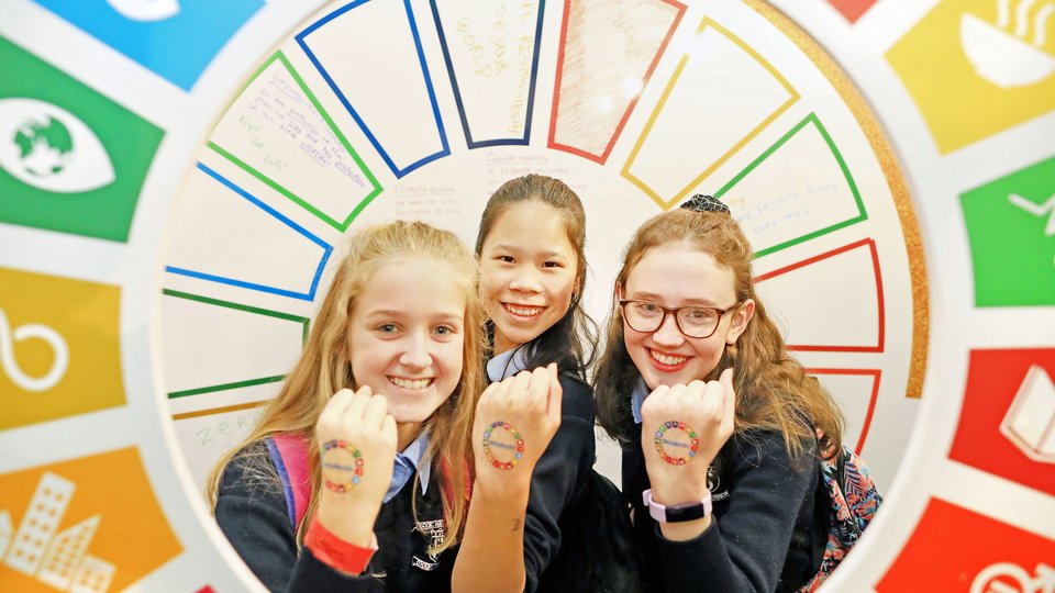 Three schoolchildren hold up their hands to show colourful transfers. Surrounding them is a circular multi-coloured arch.
