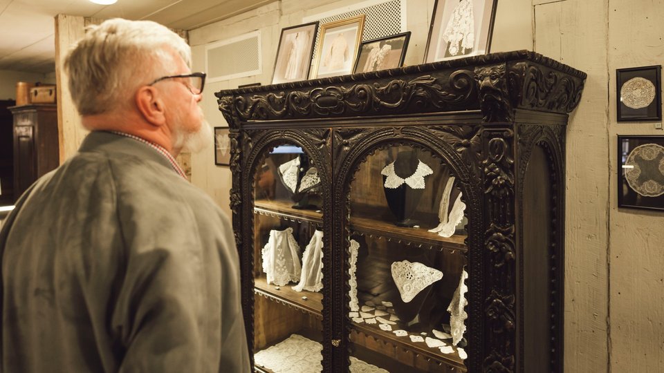 A man admires a wooden cabinet filled with Irish lace artwork