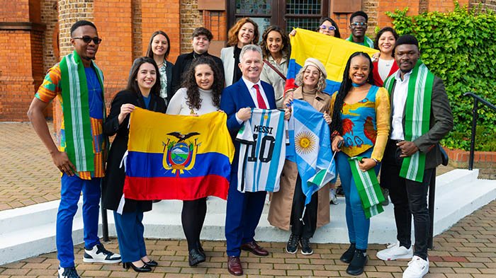 A group photo of Fellows students with the Minister, holding Latin American flags.