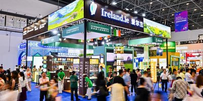 A large pavilion at an expo with Ireland written on it, crowds move in front blurred by motion.