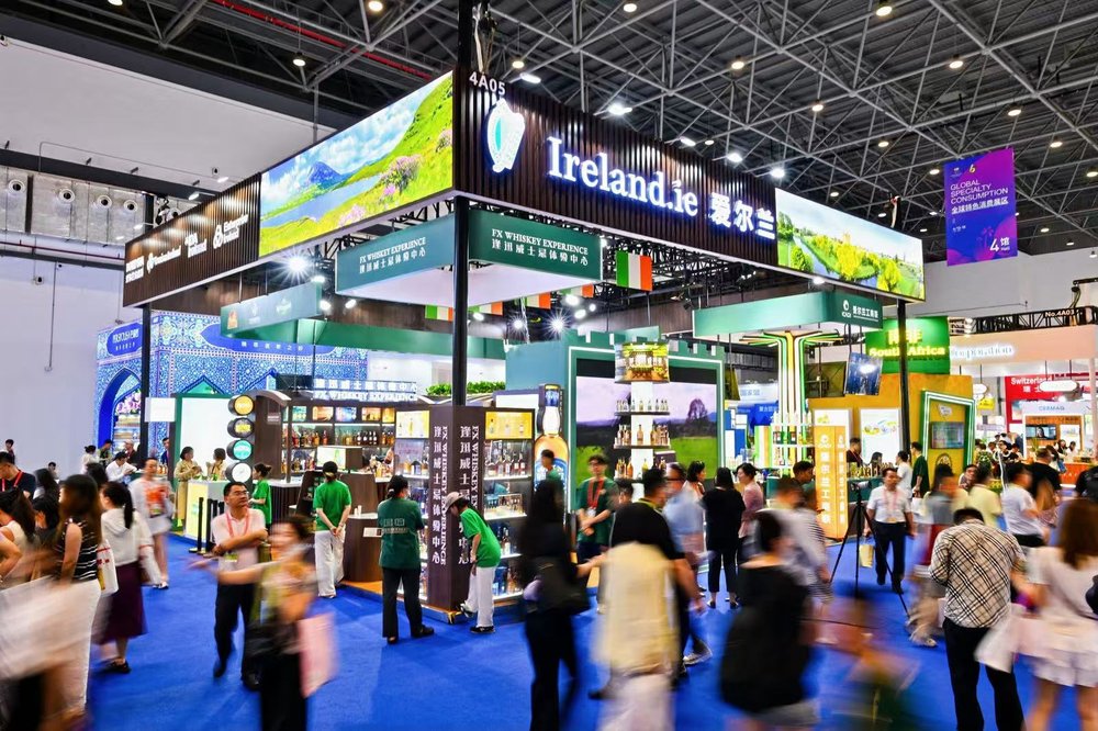 A large pavilion at an expo with Ireland written on it, crowds move in front blurred by motion.