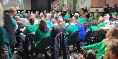 Photo of attendees wearing green sitting in chairs facing a stage.