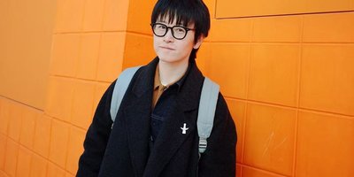 Headshot of literary creator Wuya Li standing against an orange wall