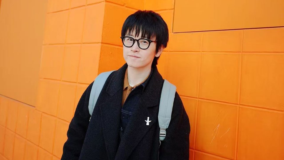 Headshot of literary creator Wuya Li standing against an orange wall