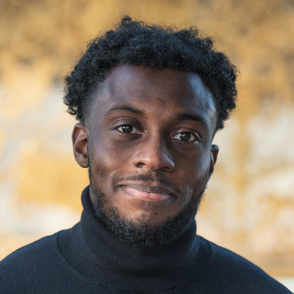 A headshot of Joel Olympio smiling and wearing a black polo neck top