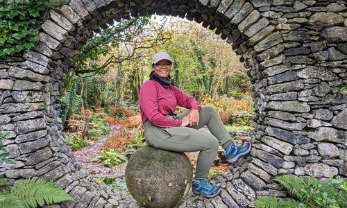 woman in hiking gears sitting in a circular opening in an old stone wall