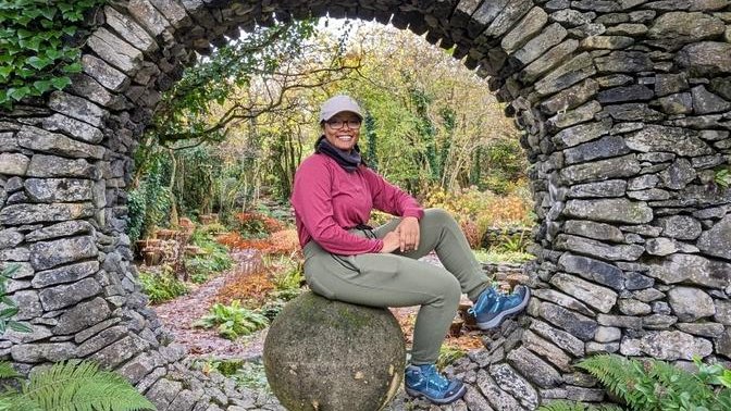 woman in hiking gears sitting in a circular opening in an old stone wall