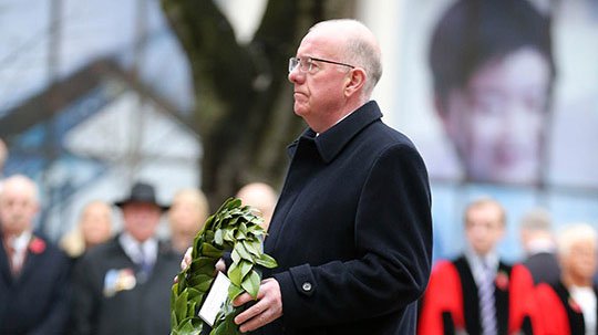man holding a wreath at a commemoration with crowd in the background