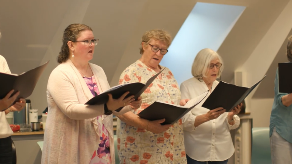 a choir of women standing in a line singing with songbooks in their hands