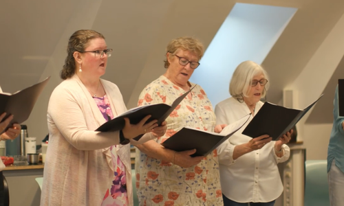 a choir of women standing in a line singing with songbooks in their hands
