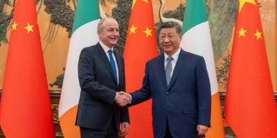 Taoiseach Micheál Martin shakes hands with President Xi Jinping in front of alternating Chinese and Irish flags.