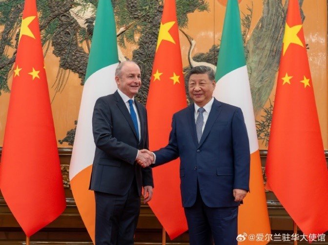 Taoiseach Micheál Martin shakes hands with President Xi Jinping in front of alternating Chinese and Irish flags.