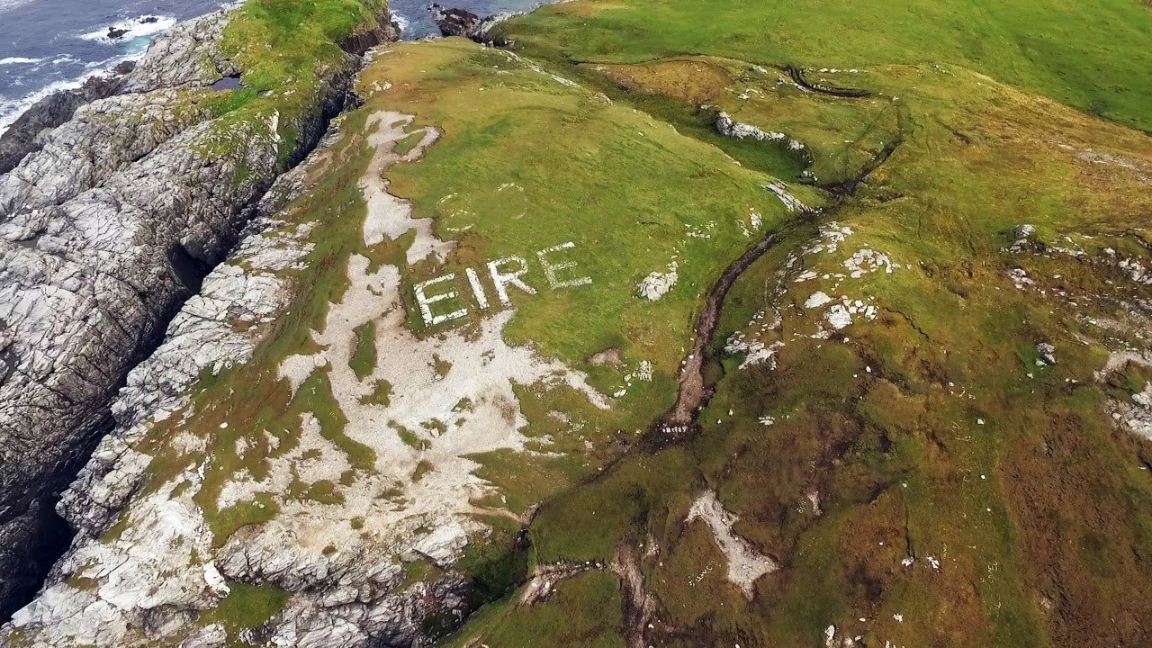 Luftansicht einer irischen Küste mit ‘Éire’ in weiβer Schrift auf dem Boden.